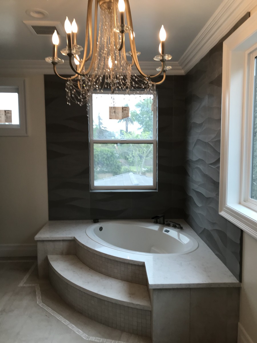 Primary bathroom with a corner soaking tub, textured feature wall and a crystal chandelier